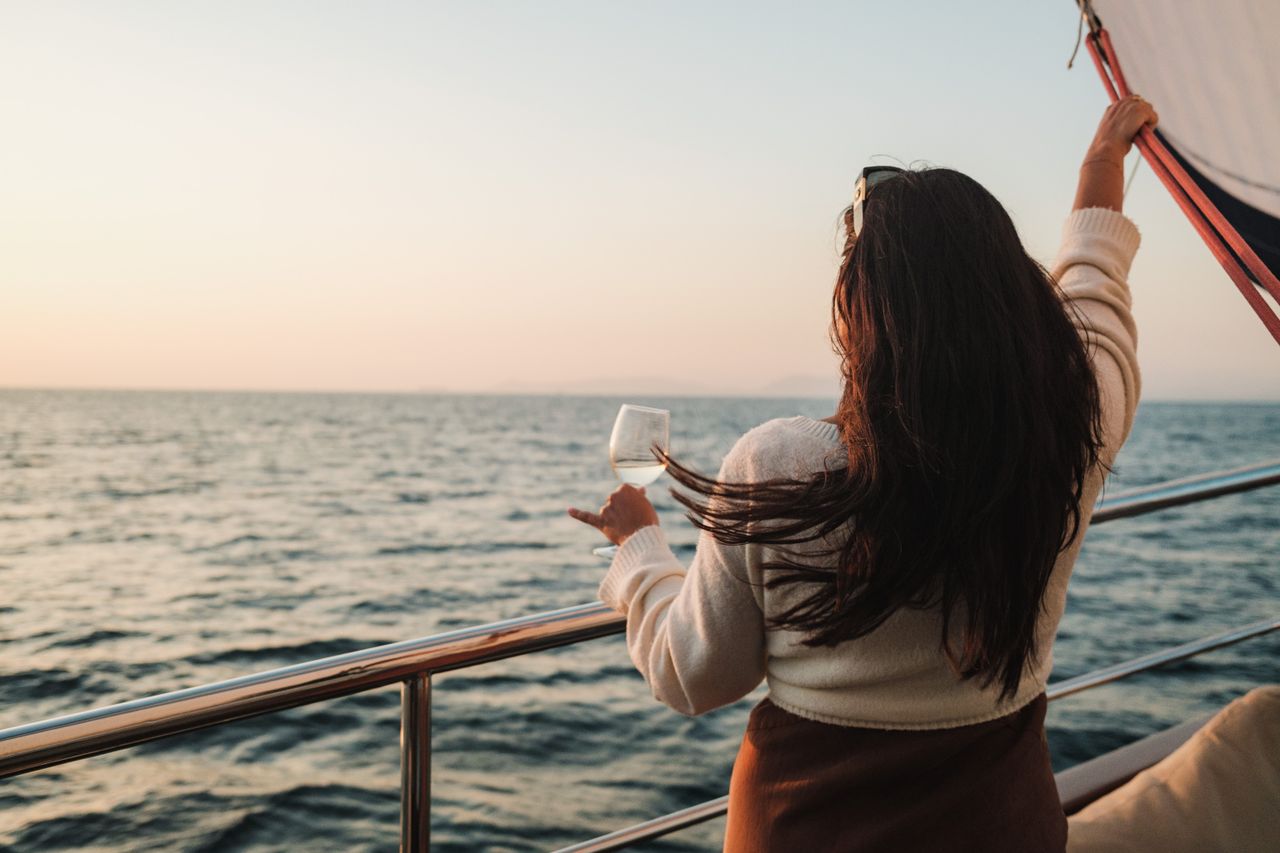 services-02 A woman with long brunette hair enjoys a drink while sailing at sunset.