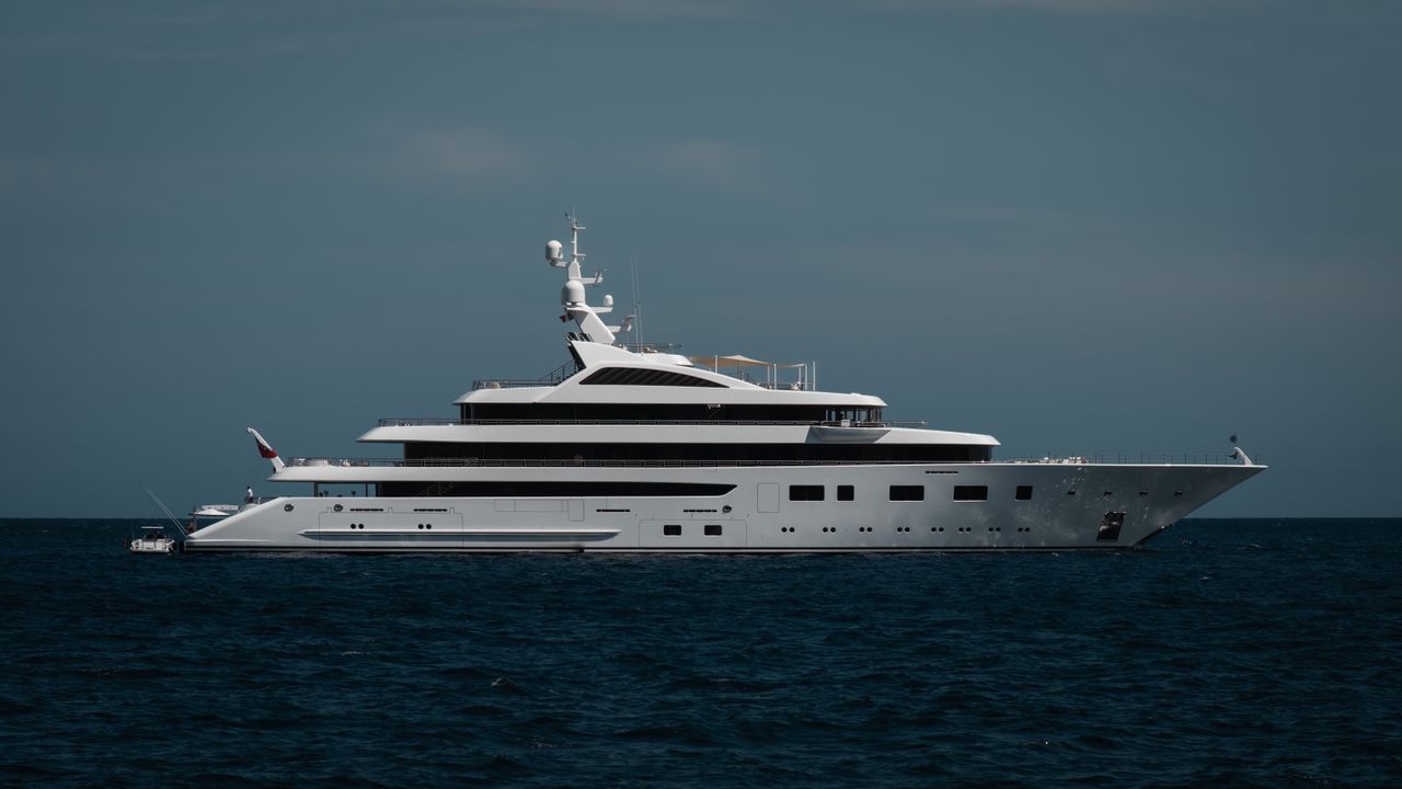 hero-img-02 A sleek luxury yacht cruising on the calm open ocean under a clear sky.